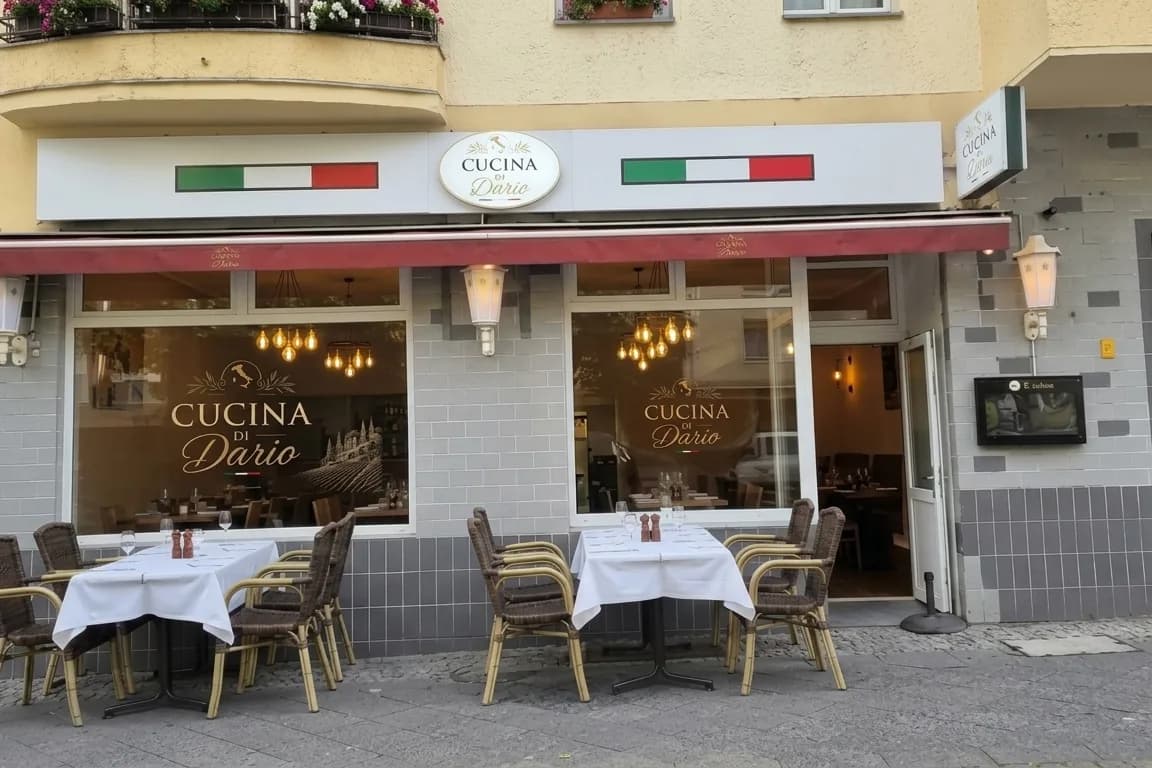 Fassade der Cucina di Dario in der Neuen Kantstraße 19 mit Markise, Trikolore und eingedeckten Tischen auf dem Gehweg