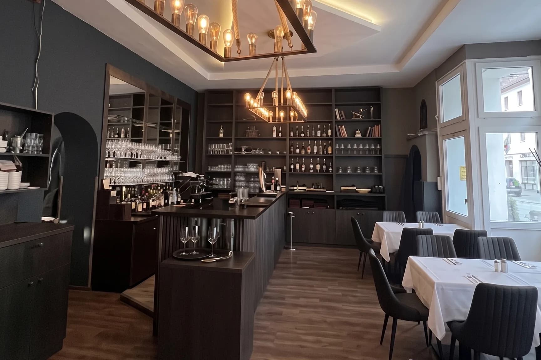Bar mit Spirituosenregal und eingedeckte Tische am Eckfenster