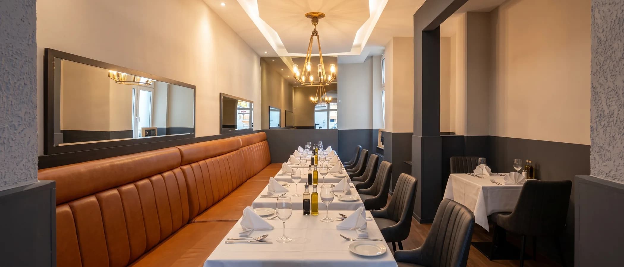 Lange Tafel an der Lederbank im Gastraum, eingedeckt mit Gläsern, Servietten, Olivenöl und Essig für eine Gruppe